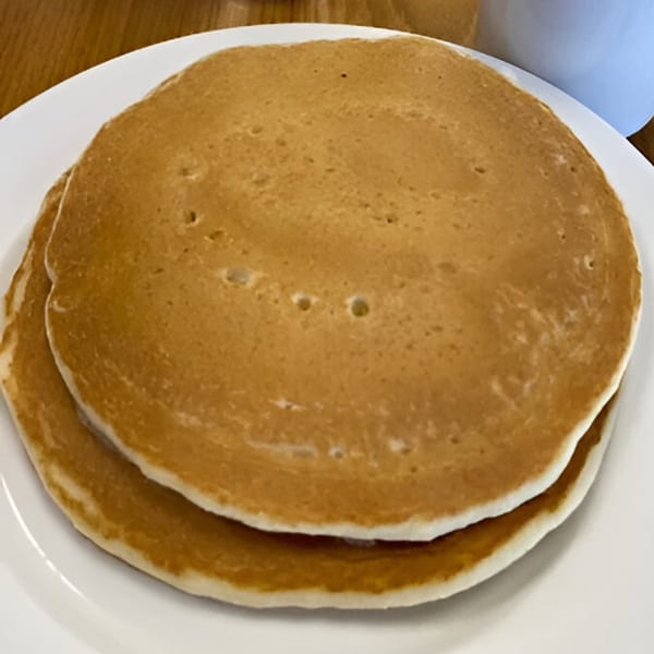Two golden-brown pancakes stacked on a white plate, ready for a delicious breakfast.