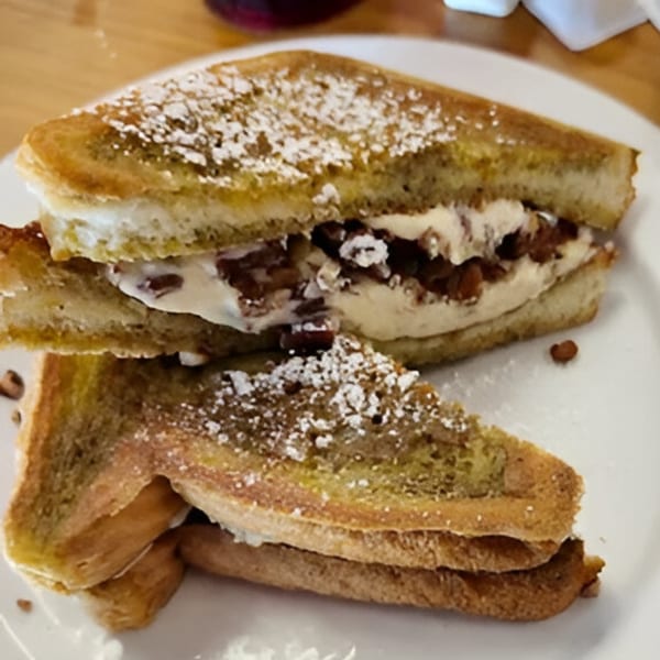 French toast sandwich with creamy filling and pecans, dusted with powdered sugar on a white plate.